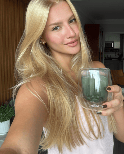 Mulher segurando copo com bebida verde.